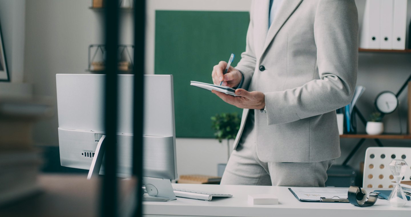 Person in a grey suit taking notes at an office desk.